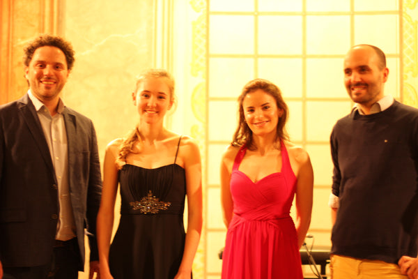 Two women and two men posing together in formal attire against a yellow wall.