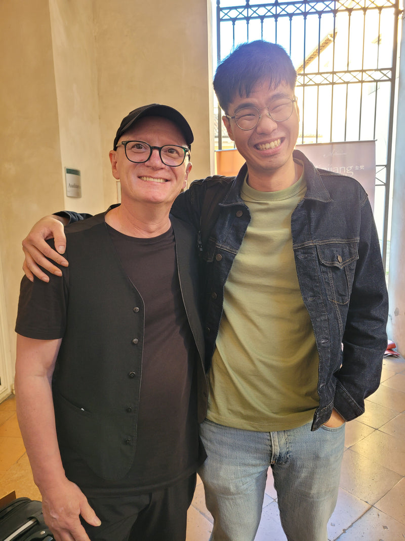 Two people standing close together indoors with a neutral background