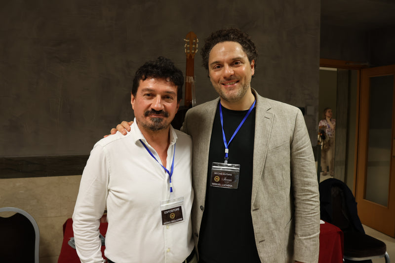 Two men standing together with a guitar in the background