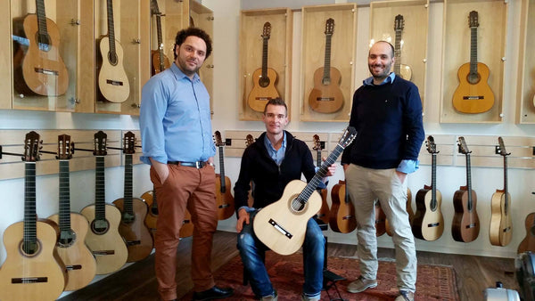 Three men posing with a guitar in a room filled with guitars