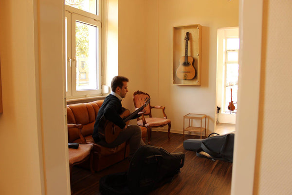 Person playing guitar in a room with a couch and window